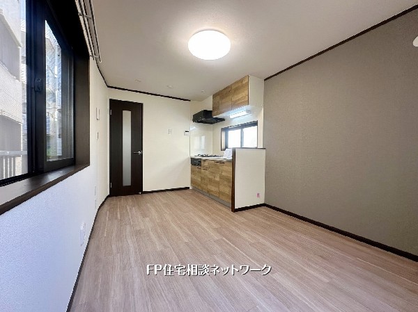 窓面が広く、自然光がやさしく届くLDK。木目調キッチンとアクセントクロスが調和し、家具レイアウトもしやすいシンプルで心地よい空間です。